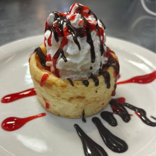 A Baked dessert with whipped cream, chocolate, and raspberry drizzle in a pastry cup.