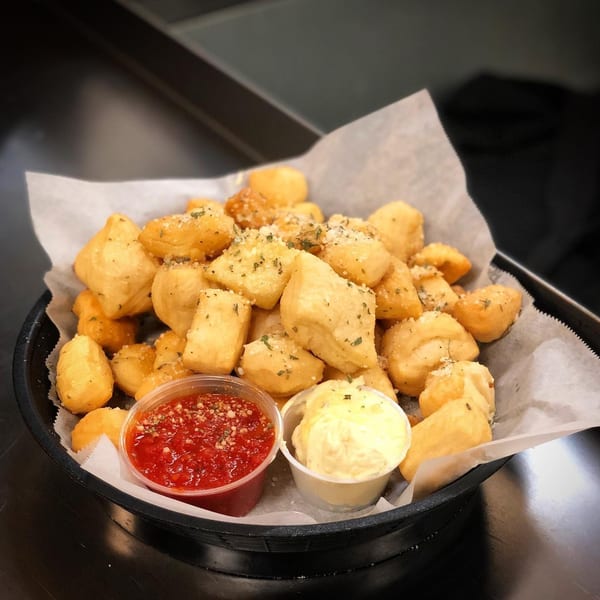 A basket of golden-brown pizza dough nuggets, sprinkled with herbs and parmesan, served with marinara and garlic butter.
