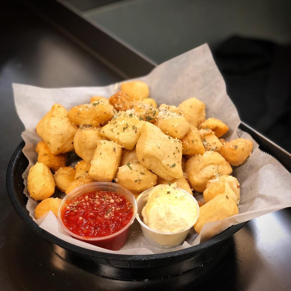 A basket of golden-brown pizza dough nuggets, sprinkled with herbs and parmesan, served with marinara and garlic butter.