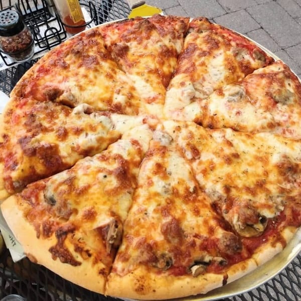 A whole Buddyz pizza, cut into slices, with melted cheese and toppings, on a metal table.