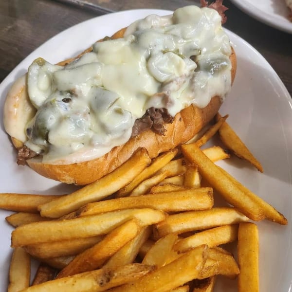A Baked Philly cheesesteak sandwich with melted cheese and mushrooms, served with a side of golden fries.