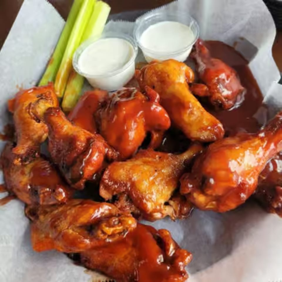 Baked's BBQ chicken wings with two cups of ranch and celery sticks in a basket.